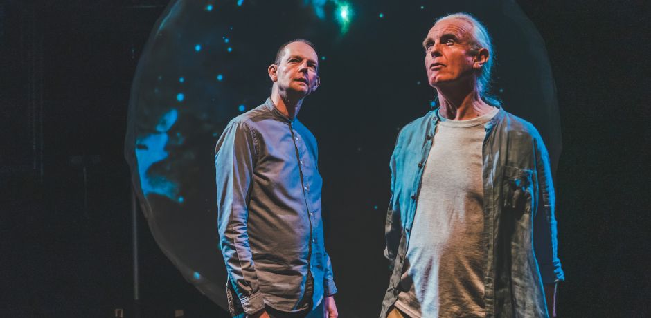 Daniel Morden and Hugh Lupton stand in front of a large disc covered in cosmic projections