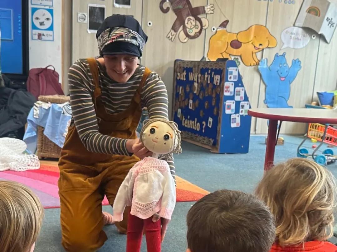 Naomi Doyle holding up a puppet in front of children in a school.