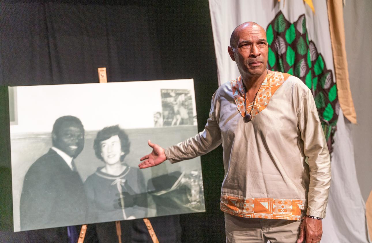 Phil Okwedy gesturing towards a large black and white photograph of his parents