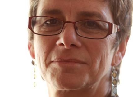 A white woman with short hair, wearing glasses, long earrings and a brown top