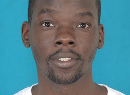 a head and shoulders photograph of John Mukeni Namai, a young black man with short hair and beard wearing a white t shirt