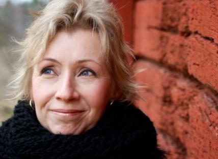 A white woman with blond hair wearing a high necked black coat