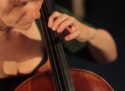 a young white woman with red hair tied back at the sides, wearing a green dress and playing the cello